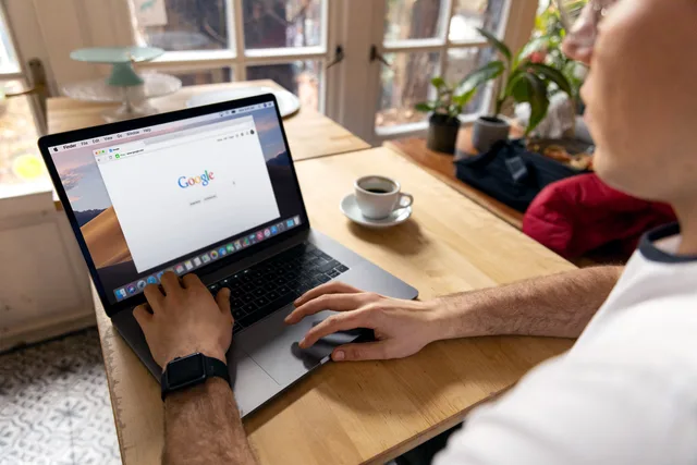 A person uses a laptop for internet browsing. A bright indoor setting with coffee on a wooden table. How to audit a PPC agency: an 8-point checklist for UK advertisers